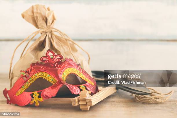 purim jewish holiday composition with purim mask and purim gragger or a noisemaker and a bag with candy on a vintage wood background with copy space - torah dressed stock pictures, royalty-free photos & images