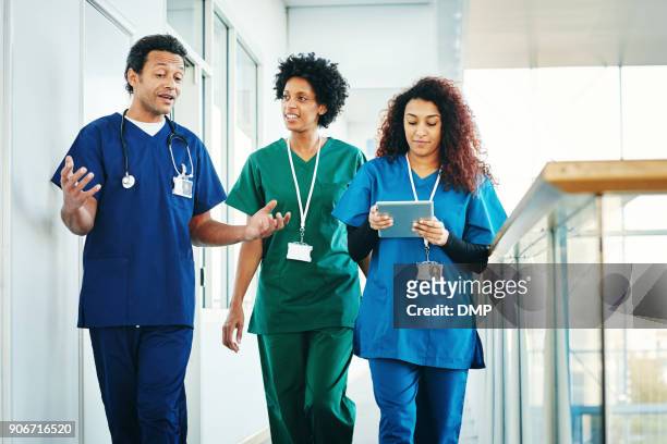 grupo de profesionales médicos discutiendo a lo largo de pasillo de hospital - vestimenta de hospital fotografías e imágenes de stock