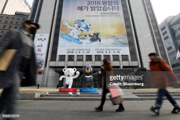 Pedestrians walk past an advertisement and statues of the 2018 PyeongChang Winter Olympic Games mascot Soohorang, left, and Bandabi, right, displayed...