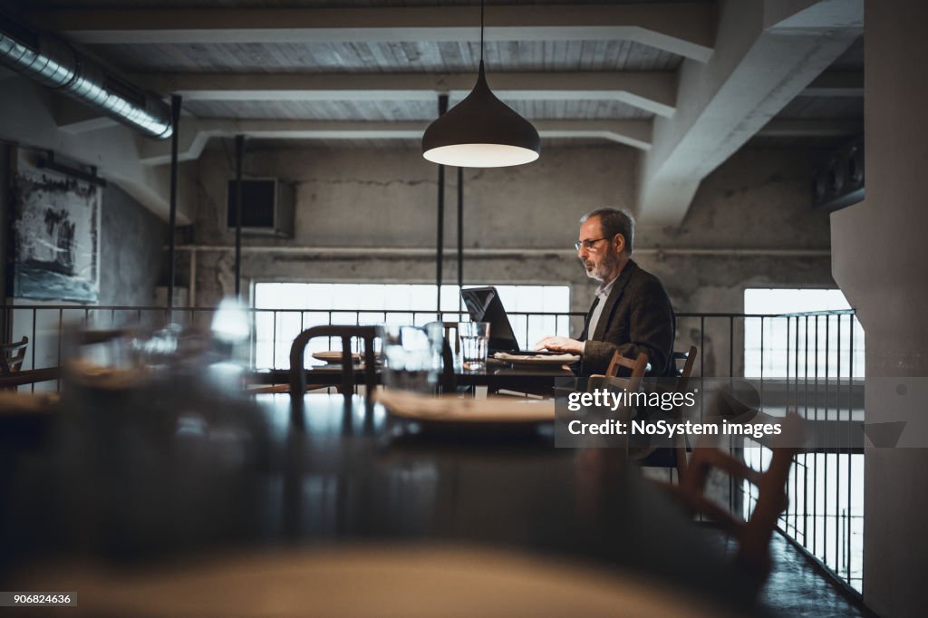 Co-Working Space in High-End Restaurants. Senior businessman with beard working on laptop in restaurant.