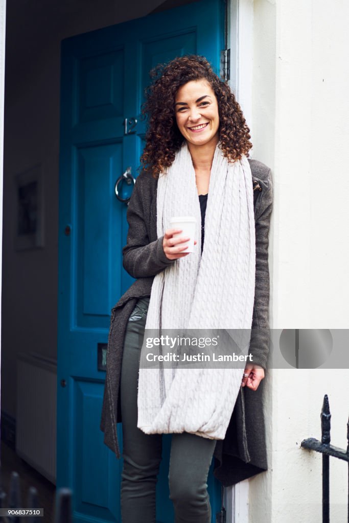 Mixed race woman stands at front door with coffee waiting for friends