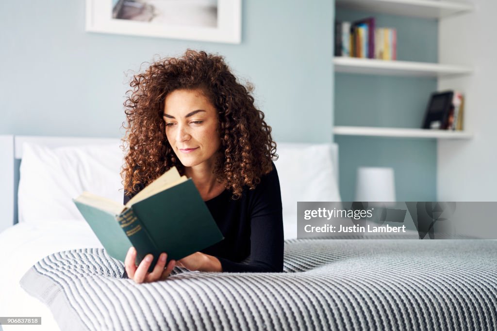 Mixed Race Woman engrossed reading a book at home on the bed in the daytime
