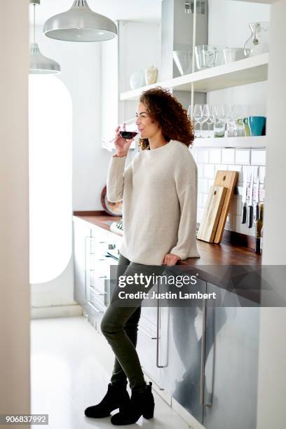 mixed race woman relaxing drinking red wine at home in kitchen - brown hair drink wine stock pictures, royalty-free photos & images