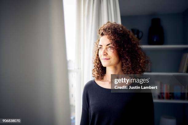 mixed race woman looking contemplatively out of bedroom window - looking through stock pictures, royalty-free photos & images