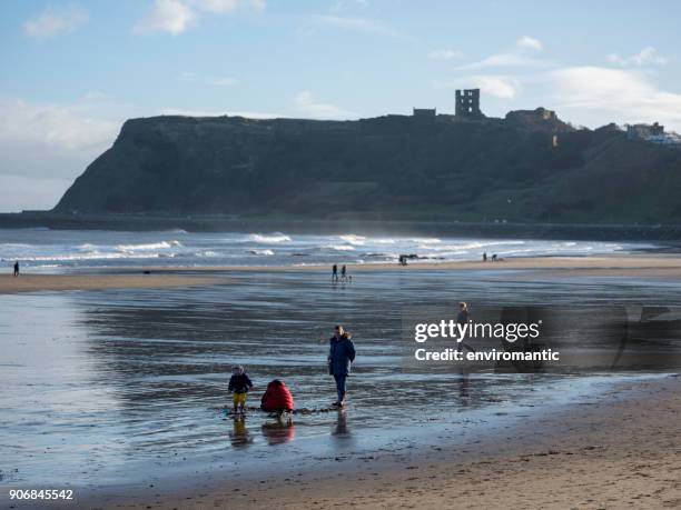 menschen spazieren gehen und spielen im sand am north marine drive in scarborough im kalten winter mit scarborough schloß im hintergrund. - north yorkshire stock-fotos und bilder