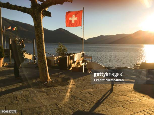 photographer taking photos on alpine lake with mountain and swiss flag - schweizer flagge stock-fotos und bilder
