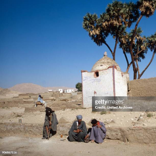 Three men sitting by a small building, Egypt 1980s.