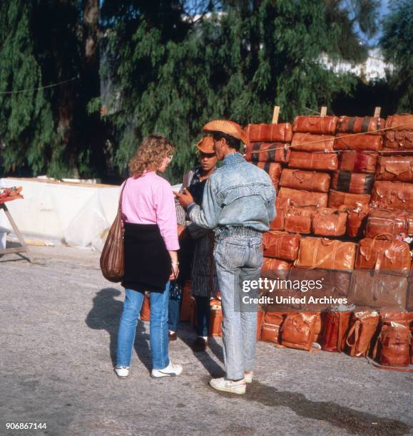 Female tourist bargaining with a vendor of leather goods at Sidi Bou Said, Tunisia 1980s.