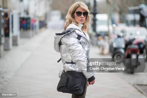 Gitta Banko wearing a silver-metallic down jacket and camouflage patterned jeans by True Religion, white cotton blouse with large, pleated sleeves...