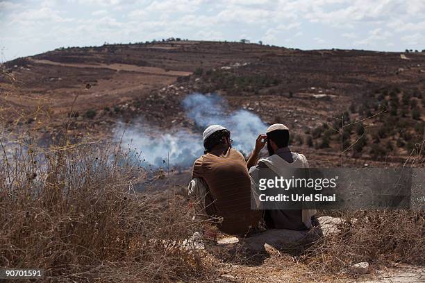 Jewish settlers sit on a hill top as a Palestinian field burns after a violent clash between settlers and Israeli security forces erupted at a West...