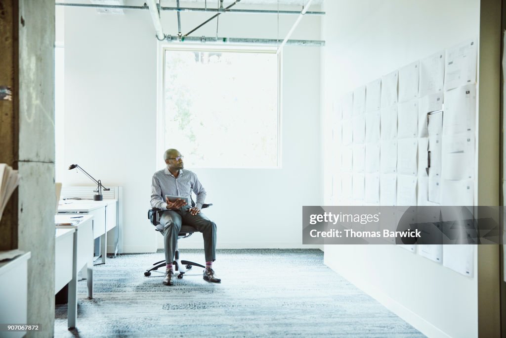Businessman reviewing project plans on office wall while working on digital tablet