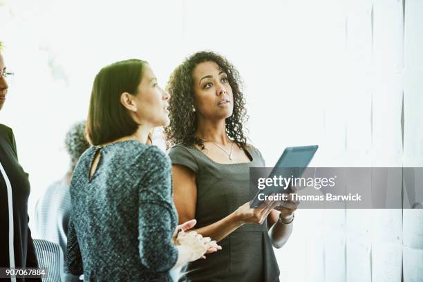 businesswomen working on digital tablet while reviewing project plans on office wall - contact list stockfoto's en -beelden