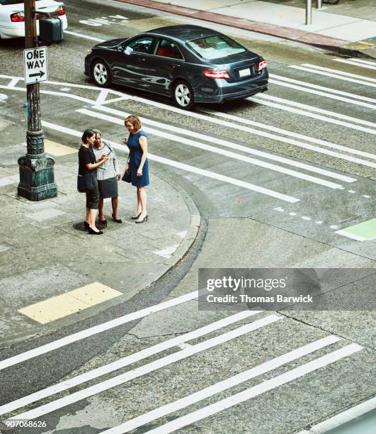 overhead view of businesswomen on street corner looking at smartphone - management car smartphone stock-fotos und bilder