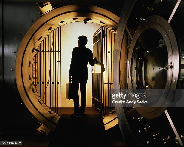 man with briefcase silhouetted in open door of bank vault - safe stock-fotos und bilder