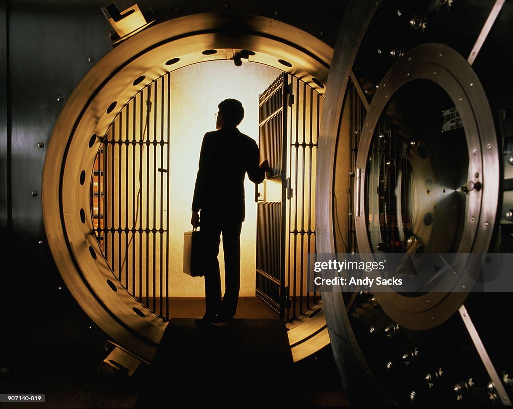 Man with briefcase silhouetted in open door of bank vault