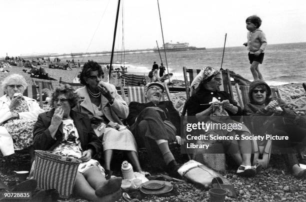 Group of elderly people relax in deckchairs on the beach at Brighton. Photographer Tony Ray-Jones created most of his images of the British at work...