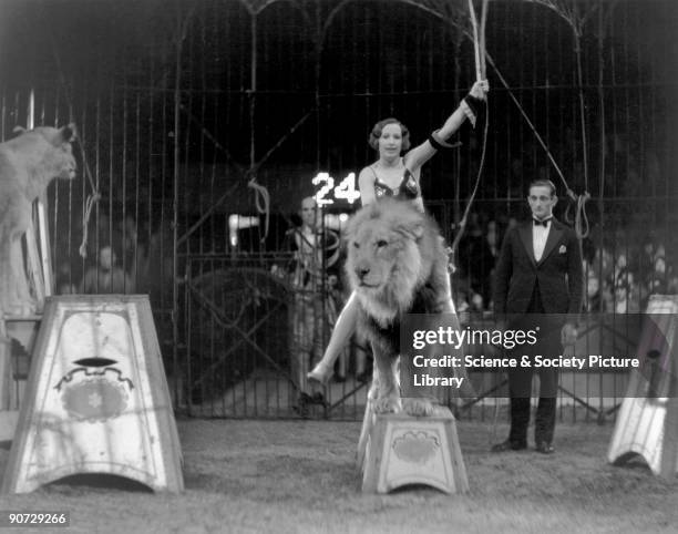 Woman lion tamer sitting on the back of a lion during a circus performance, c 1920s.