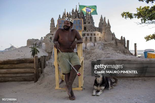 With a crown on his head, Marcio Mizael Matolias sits next to his dog - called Humana - on a throne in front of his sand castle, despite the...