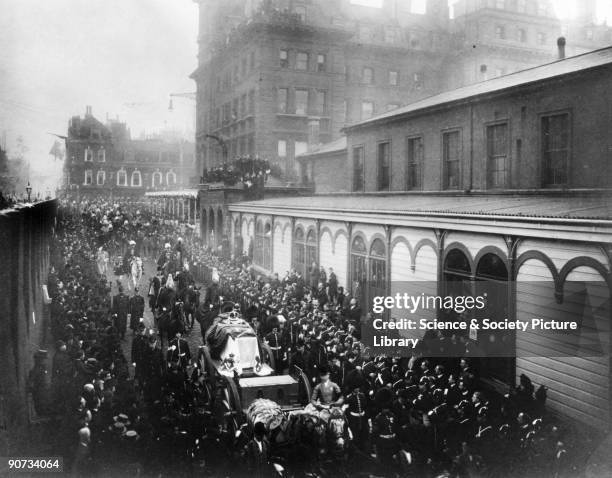 The gun carriage bearing the coffin is pulled through the London streets to Paddington Station. The coffin has been decorated with royal regalia....