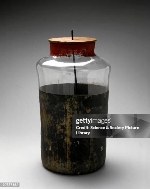 Large Leyden jar with wooden cap fitted with metal hook and short length of chain. This was a device for storing an electrical charge, or capacitor,...