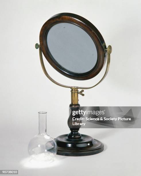 Heat is produced as sunlight is focused by a large convex lens, such as this example which is mounted on a brass pivot on a wooden stand. Heat can...