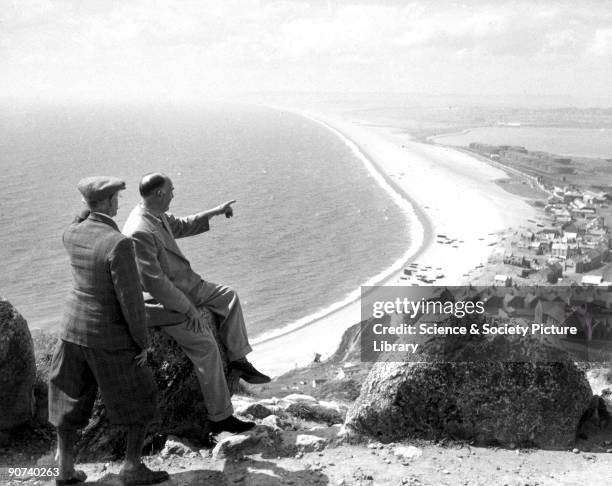 Two smartly dressed men admiring the view of a bay from the headland, c 1920s.