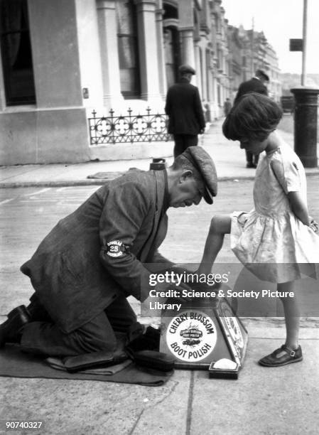 Itinerant shoeblack polishing a young girl's shoe, c 1920s.