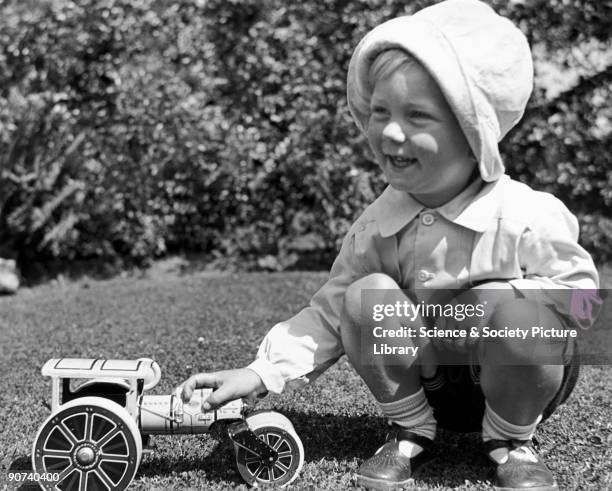 Small boy playing with a toy steamroller in a garden, c 1920s.
