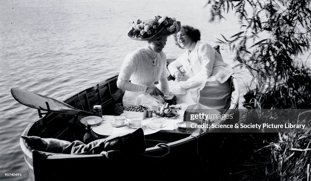 Enjoying a picnic in a rowing boat, c 1910s.