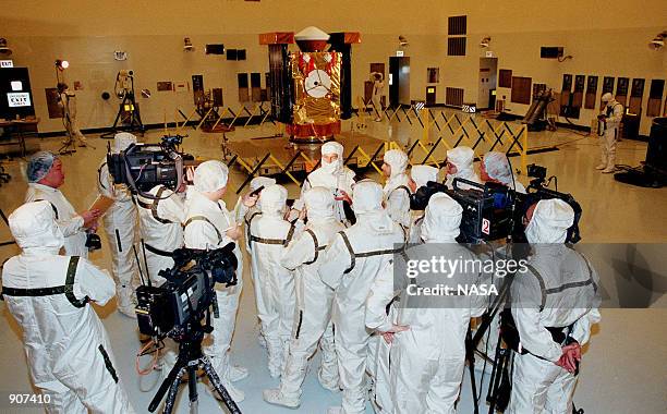 In the Payload Hazardous Servicing Facility, media representatives, dressed in protective suits, are updated by Project Manager Richard Grammier ,...