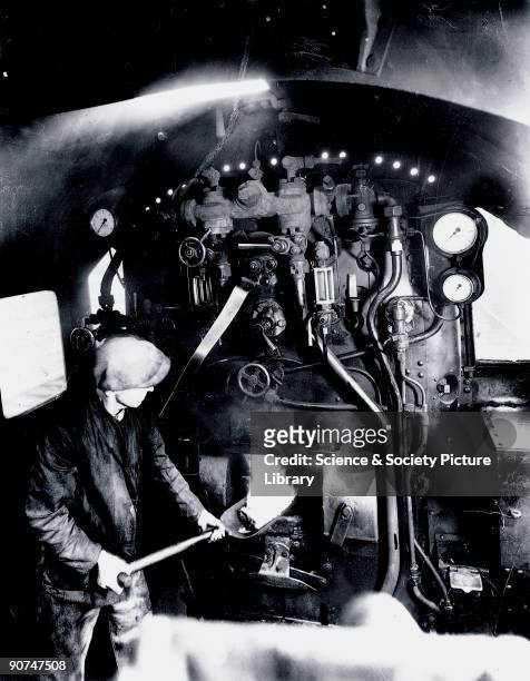 Fireman stokes the furnace in the cab of a London, Midland & Scottish Railway locomotive.