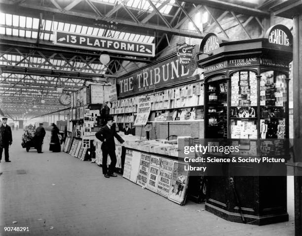 Wyman & Sons Ltd's newsagent's stand on platforms 12 and 13 at Euston station, with placards for newspapers and magazines on display, including 'The...