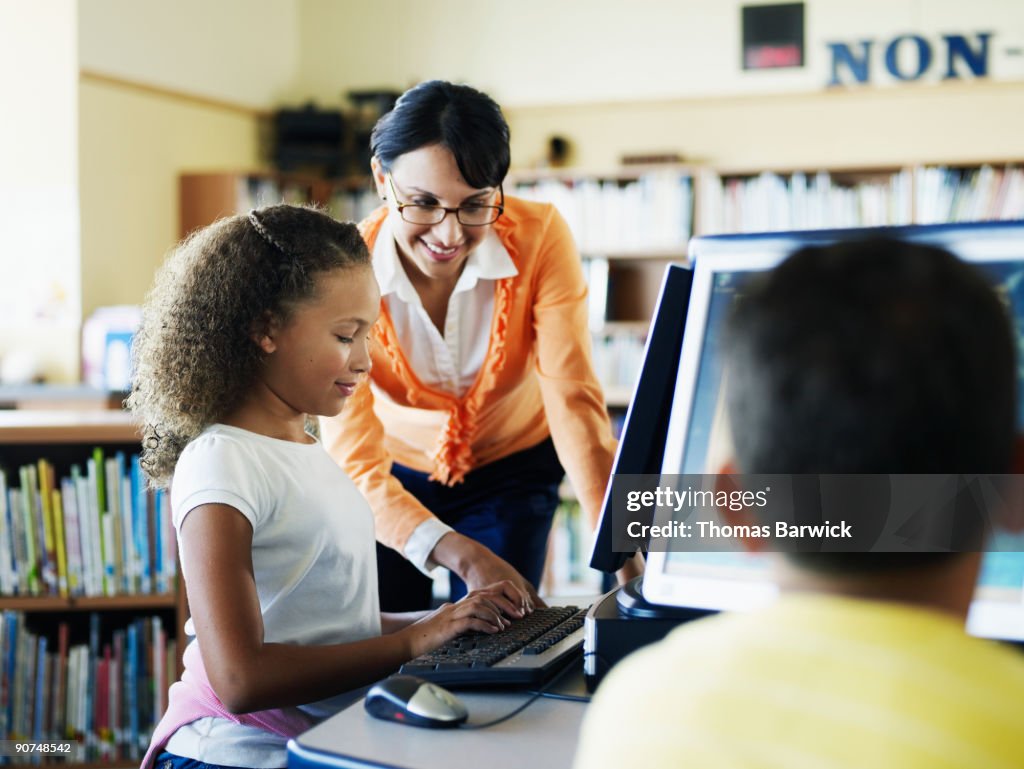 Teacher assisting female student at computer