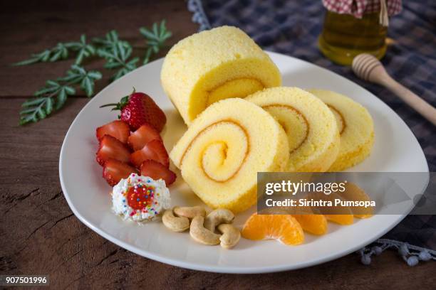 sponge cake roll with cream, strawberries and orange fruits on a white plate on wooded table background. - rollup photos et images de collection