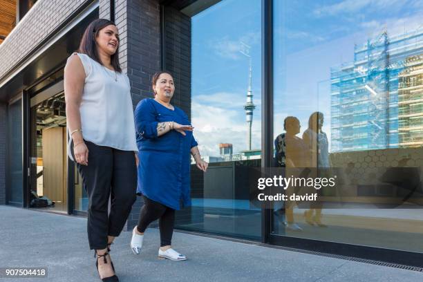 maori geschäftsfrauen zusammen spazieren, vorbei an ein modernes bürogebäude - auckland city people stock-fotos und bilder
