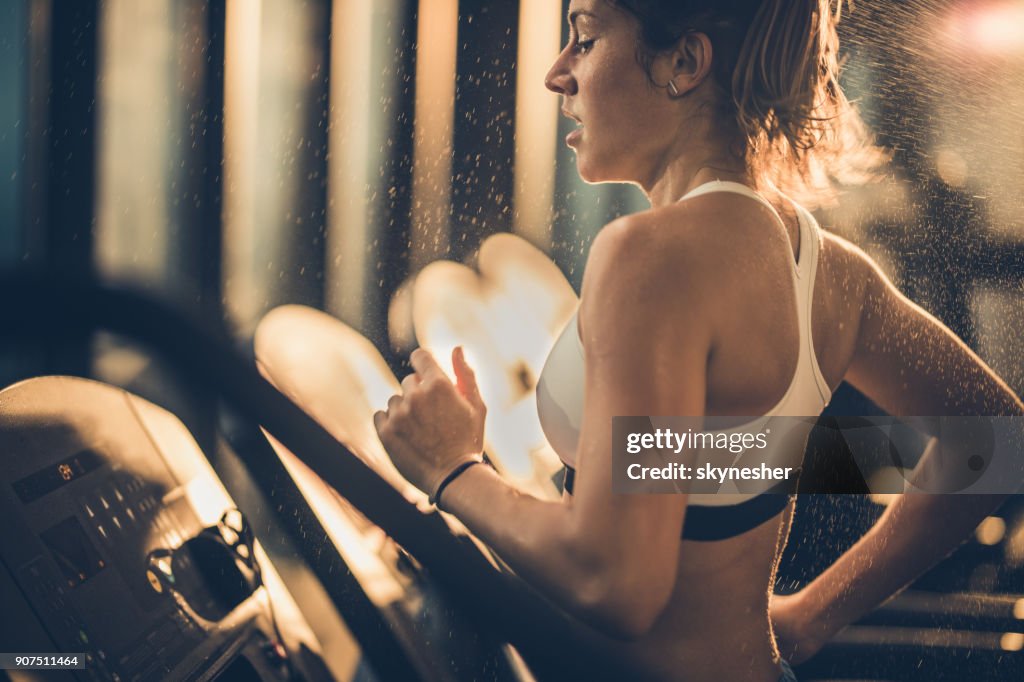 Sweaty woman running on treadmill during sports training in a gym.