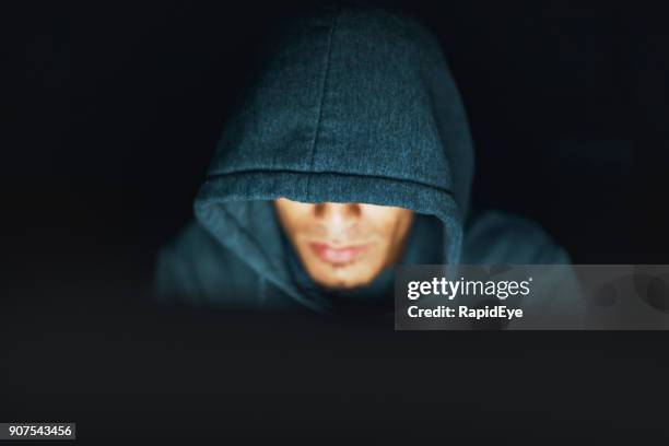 hoodie-wearing young man looks sinister, working on computer at night - illegal downloads stock pictures, royalty-free photos & images