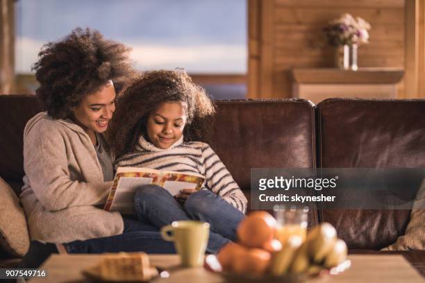 relaxed african american mother and daughter reading a book on sofa. - cosy stock pictures, royalty-free photos & images