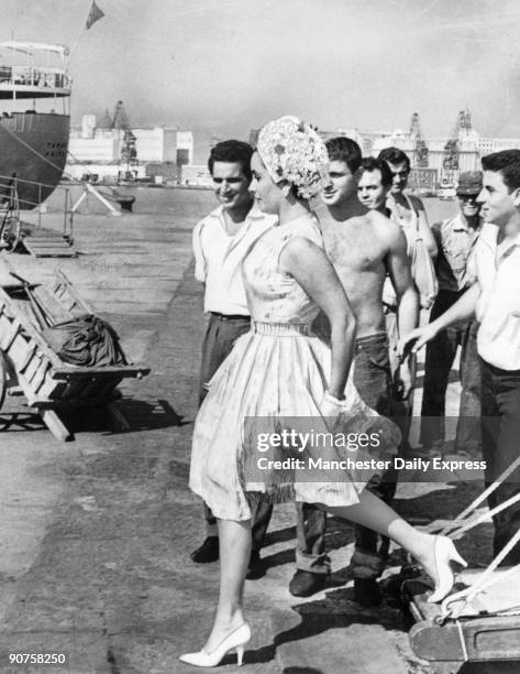 Italian dockworkers stop to admire Liz Taylor arriving from Capri for a holiday before beginning work on 'Cleopatra'.