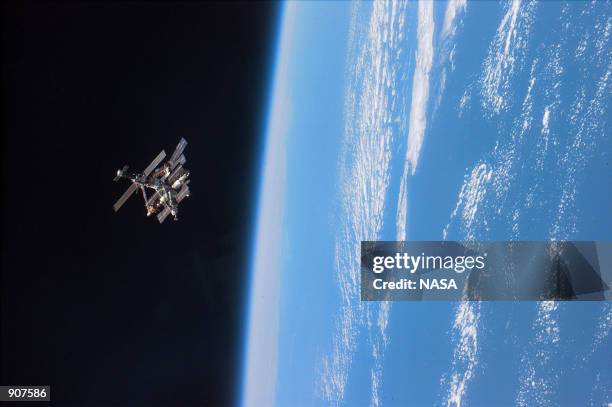 Astronauts enjoy this view of the Mir complex backdropped against the blackness of space over Earth's horizon. A thin blue line of airglow runs...