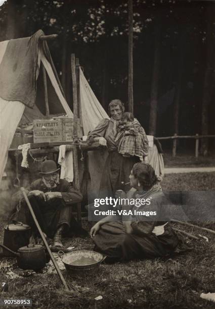 Gelatin silver print. Photograph by Horace W Nicholls of a traveller family smoking by a camp fire. They are possibly at the Derby horse race in...