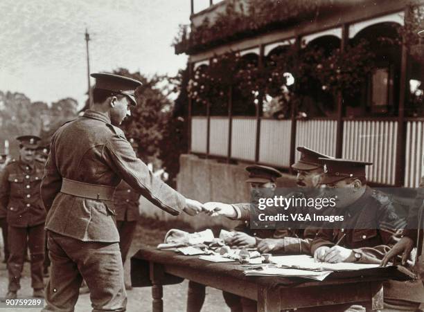 Photograph by Horace W Nicholls. A group of officers and NCOs sit at a table, possibly giving out chits or pay to the men. "
