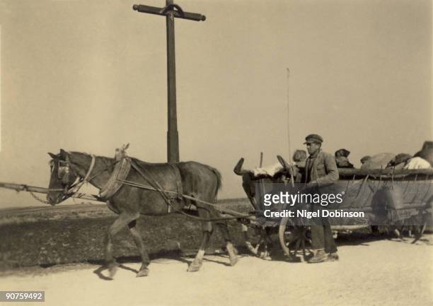 Russian civilians displaced by the War travel by horse and cart. They are passing a cross with a small crucifix on it.