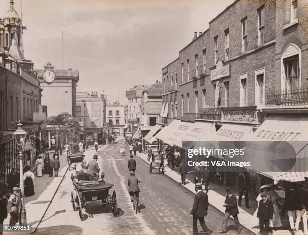 Photograph by Horace W Nicholls of shops including H Bensted, music seller; the Spread Eagle pub with beers from Watney Coombe Reid; a hairdresser; E...
