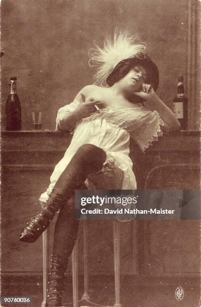 Early French postcard showing a bar girl or prostitute flanked by an absinthe bottle. She is enjoying the twin vices of smoking and drinking, while...