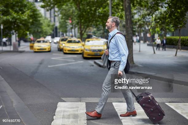 businessman walking with wheeled luggage on street - australia taxi stock pictures, royalty-free photos & images