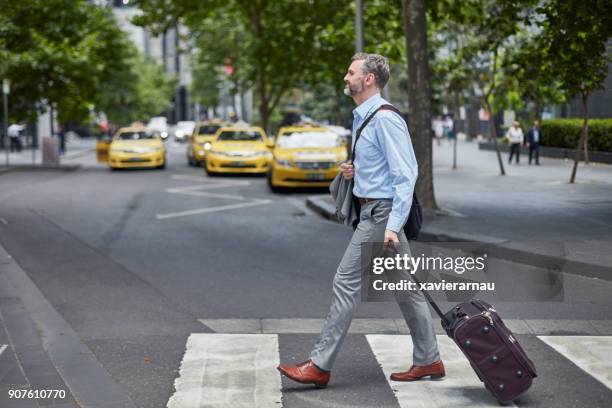 businessman walking with wheeled luggage on street - taxi melbourne stock pictures, royalty-free photos & images