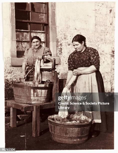 Photograph by Frank Meadow Sutcliffe . Working outside using large wooden tubs, one woman wrings the washing by hand whilst the other operates a...