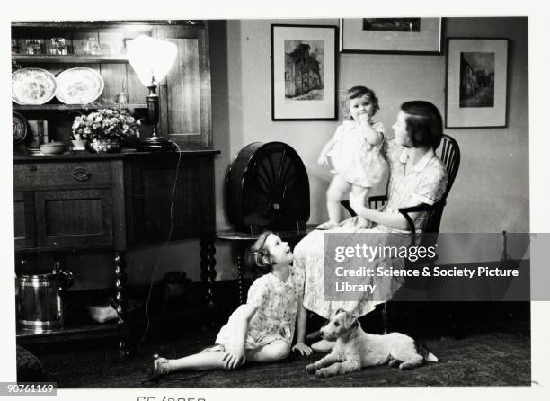 Snapshot photograph of a mother and her children listening to the radio, taken by an unknown photographer in about 1930. Originally a shooting term,...