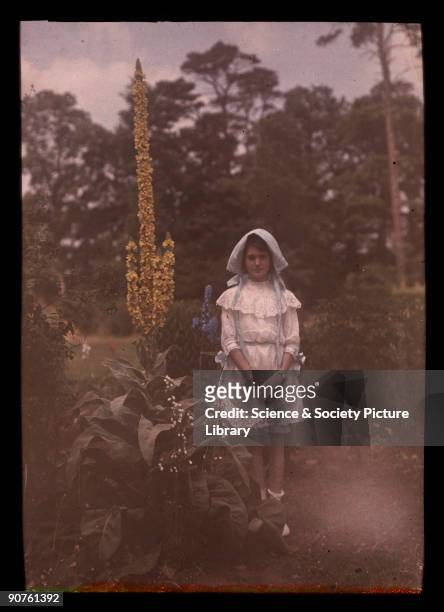 An autochrome of her daughter wearing a bonnet and lace dress, standing in a garden, taken by Etheldreda Janet Laing. In the summer of 1908 Laing...